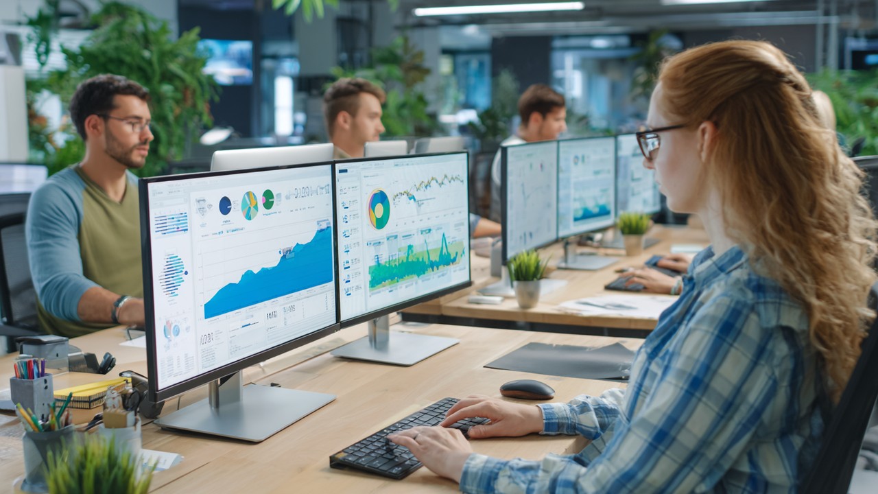 Dinamik ofis ortamında ekip, büyük monitörlerde yükselen SEO grafiklerini ve web sitesi performansını analiz ediyor.