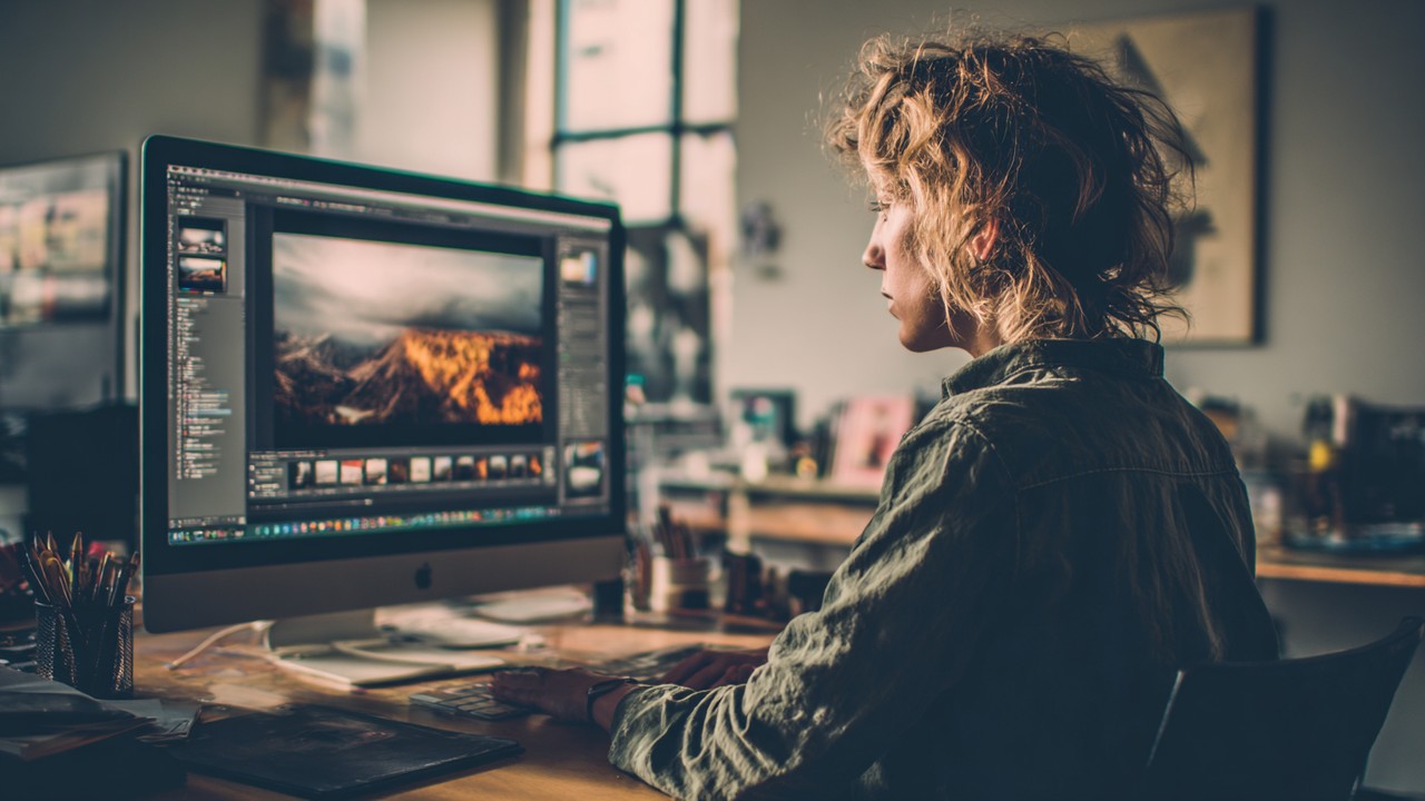 Yüksek çözünürlüklü monitörde fotoğraf düzenleme yazılımıyla görüntü boyutlandırma ve kırpma yapan grafik tasarımcı.